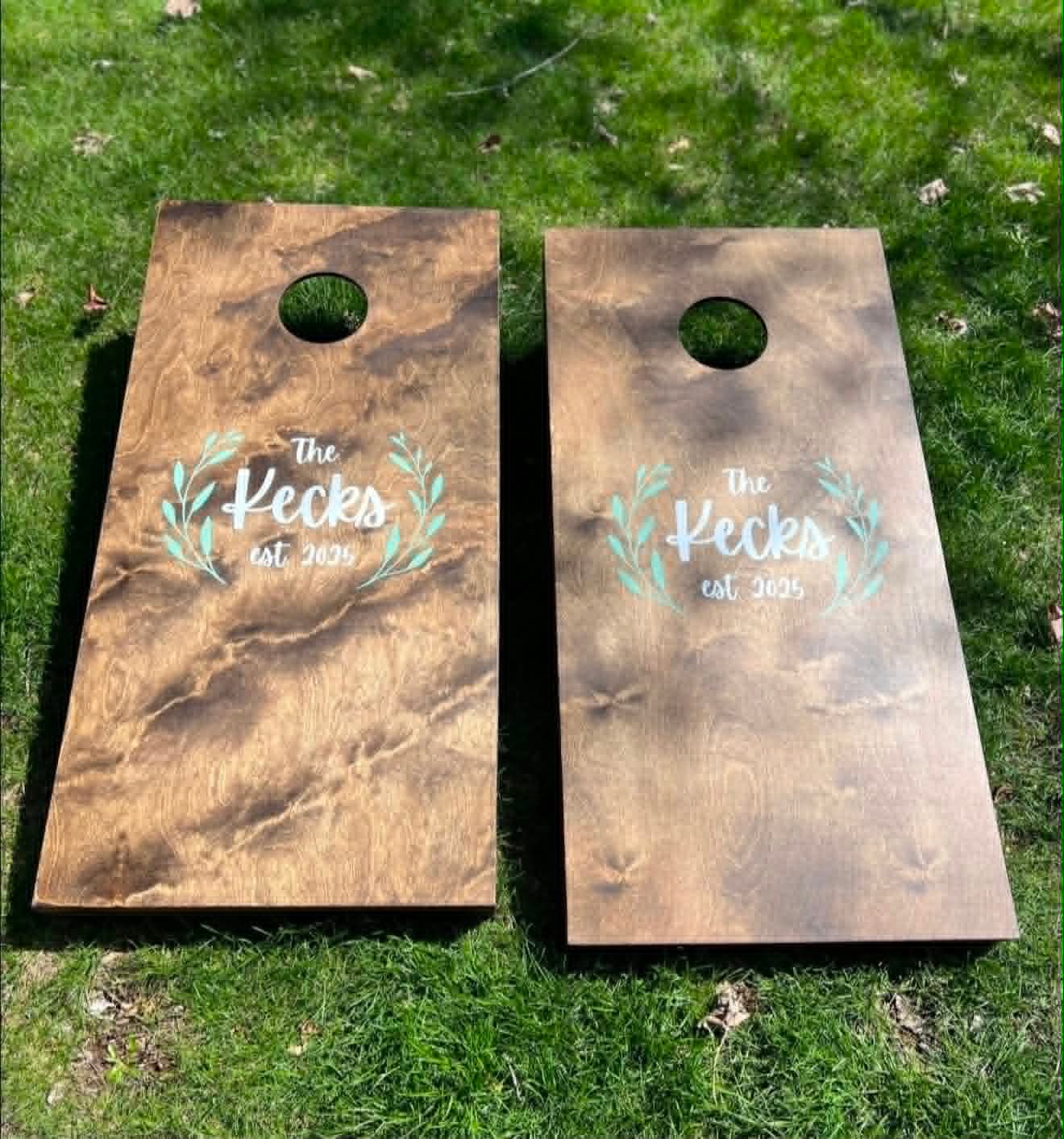 Stained wood cornhole board set reading The Kecks Est. 2025 with a leaf wreath design