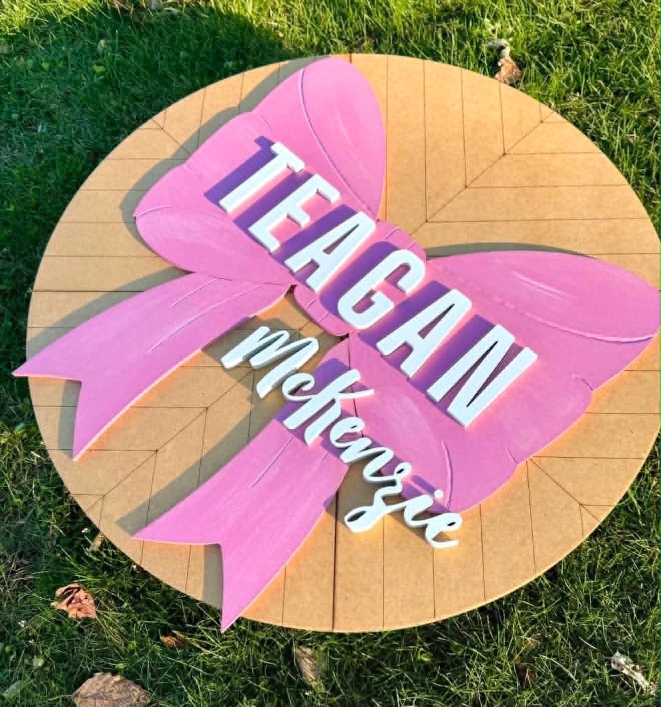 Round sign shaped like a painted pink bow reading Teagan McKenzie